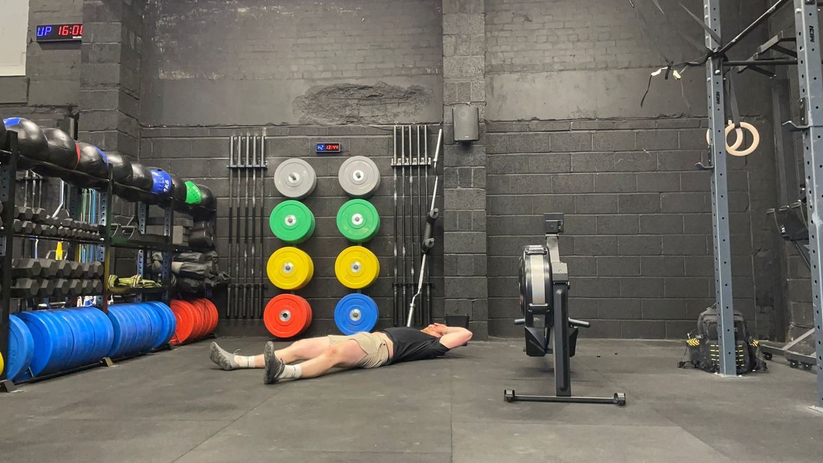 TechRadar fitness writer Harry Bullmore lying down next to a rowing machine after finishing a 2K row